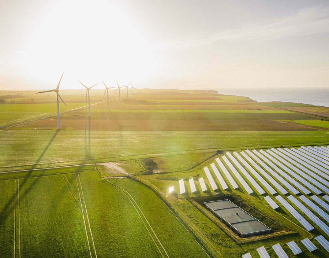 Aerial view of wind turbines and solar panels on a green meadow in bright sunlight.